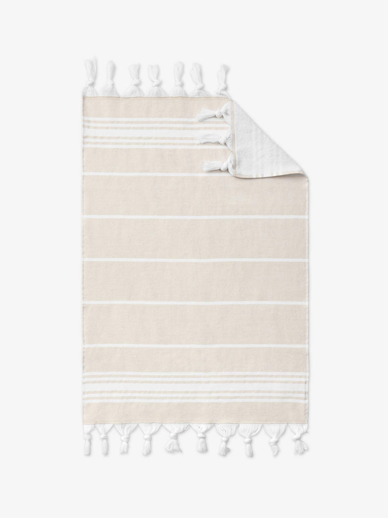 An oversized, tan and white striped Turkish cotton hand towel with white fringe laid out.