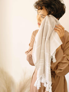 A woman drying her face with a tan and white striped Turkish hand towel.