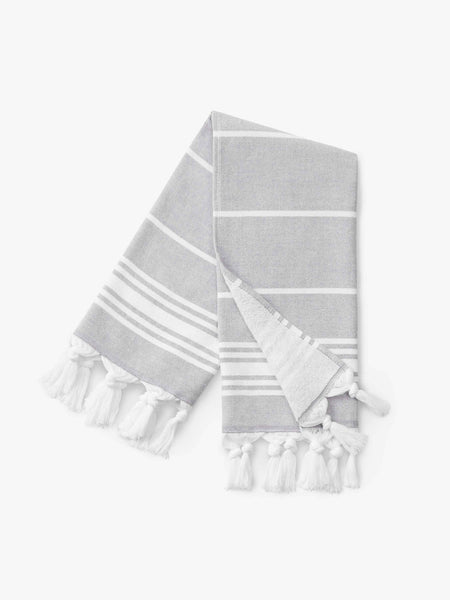 A folded stone and white striped Turkish hand towel with white fringe.