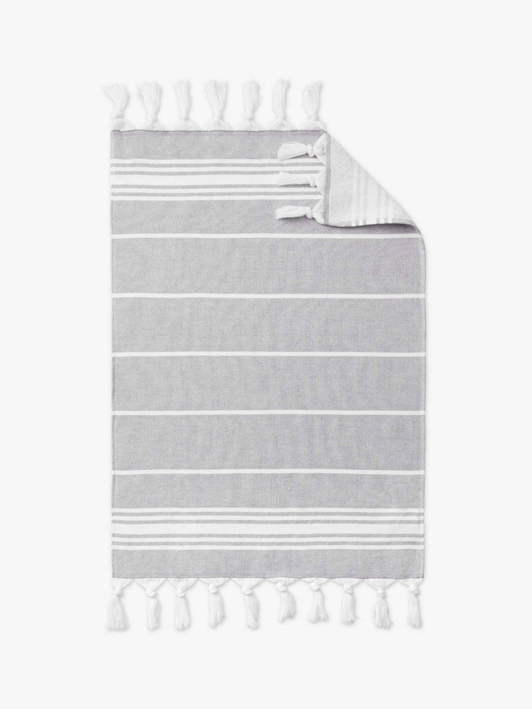 A stone gray and white striped Turkish cotton hand towel with white fringe laid out. 