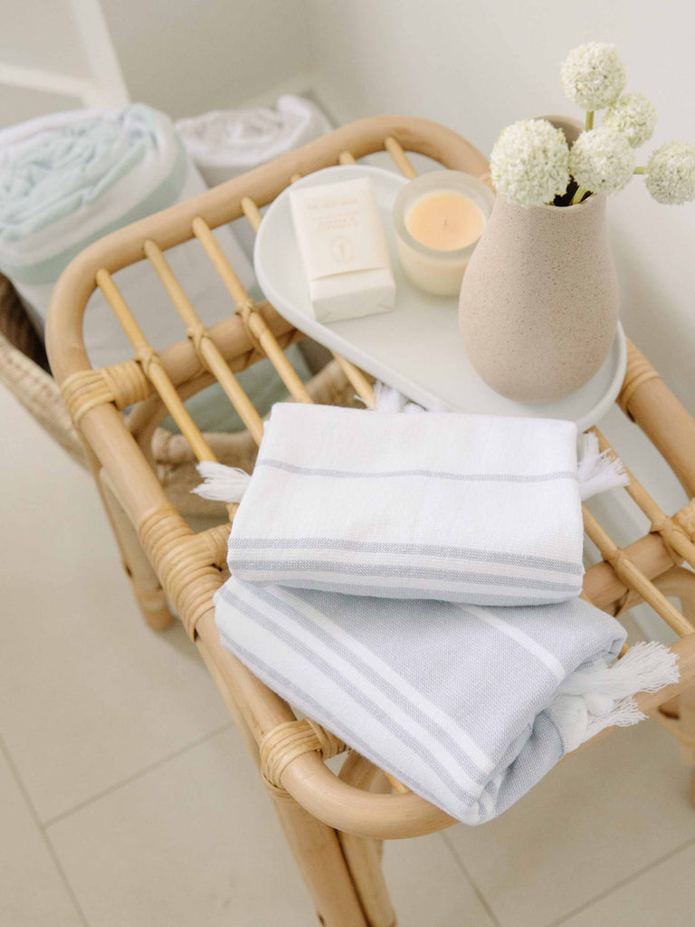 Two grey and white striped hand towels folded over an end table with a candle.