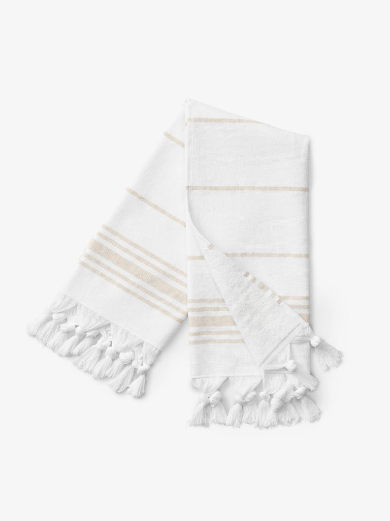 A folded tan and white striped Turkish hand towel with white fringe.