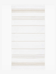An oversized tan and white striped Turkish cotton towel with white fringe laid out.