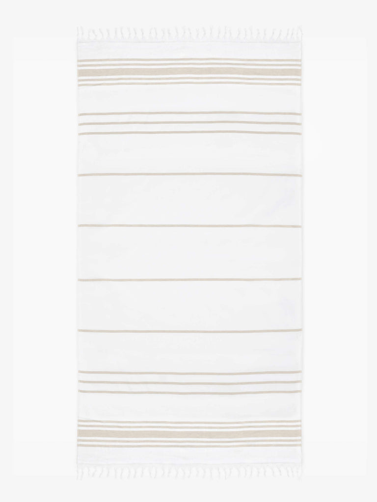 An oversized tan and white striped Turkish cotton towel with white fringe laid out.