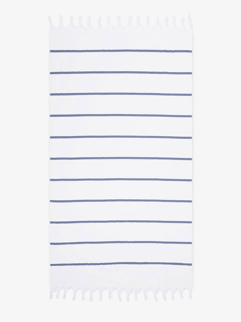 An oversized, navy and white striped Turkish cotton towel with white fringe laid out.