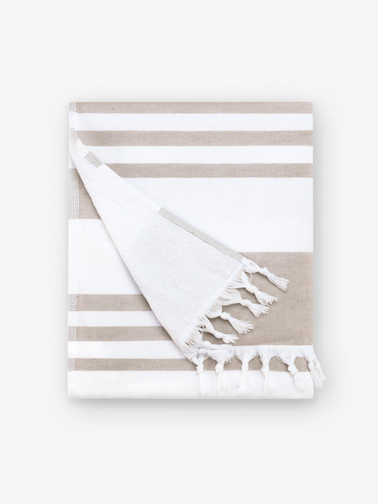 A folded tan and white striped Turkish towel with white fringe.
