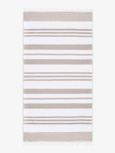An oversized, tan and white striped Turkish cotton towel with white fringe laid out.