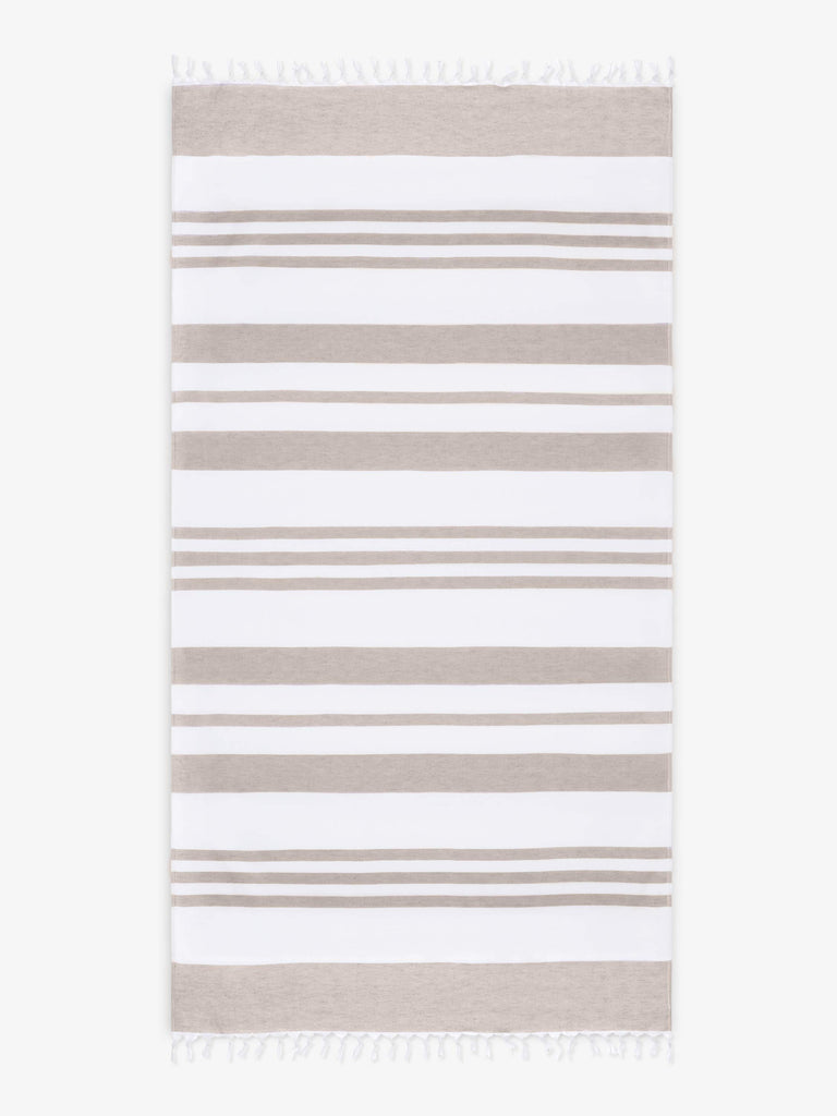 An oversized, tan and white striped Turkish cotton towel with white fringe laid out.