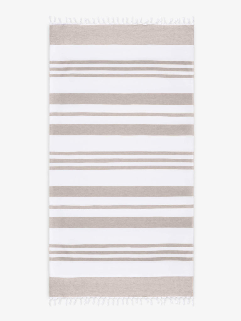 An oversized, tan and white striped Turkish cotton towel with white fringe laid out. 