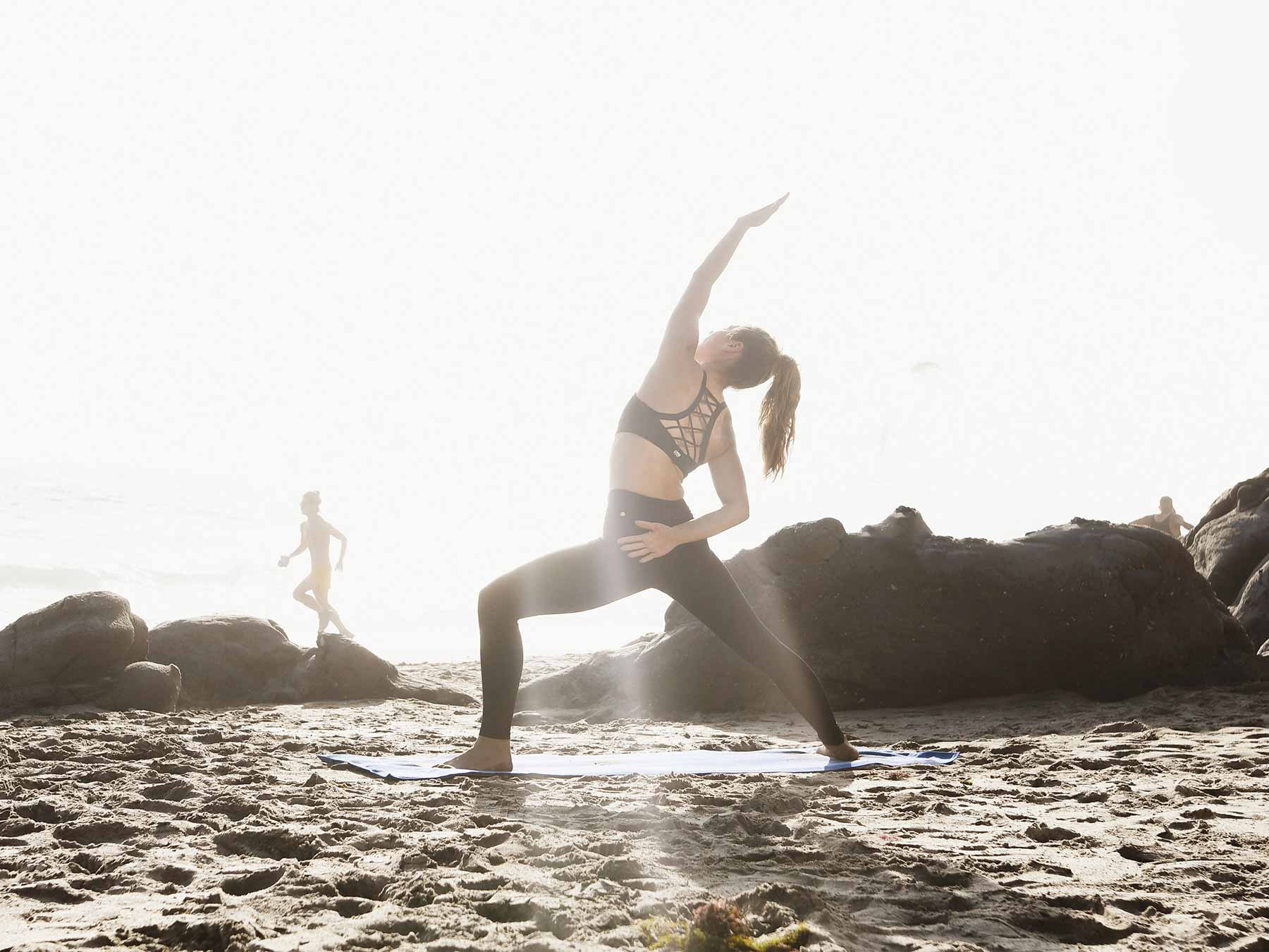 Young woman on a California beach doing yoga on top of a yoga mat towel.