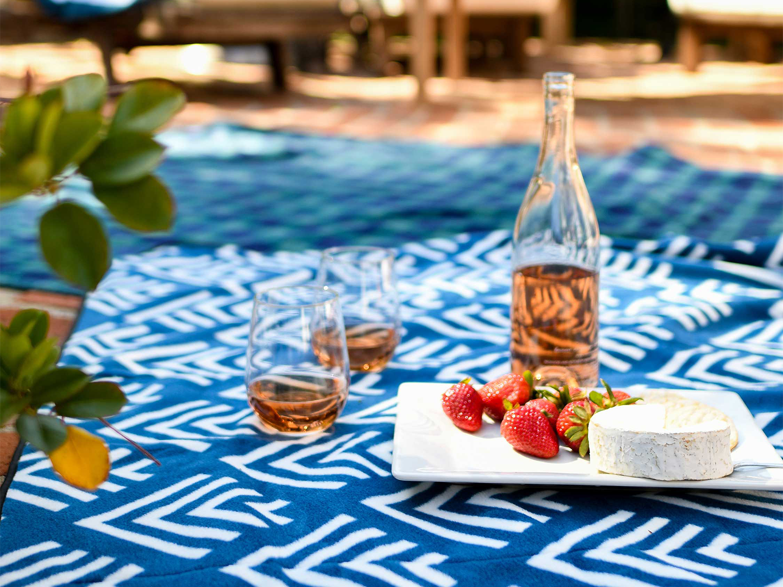 A picnic set up with cheese, strawberries, and wine on a blue picnic blanket