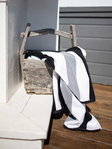 A black, gray, and white striped cabana beach towel hanging over a wooden basket.