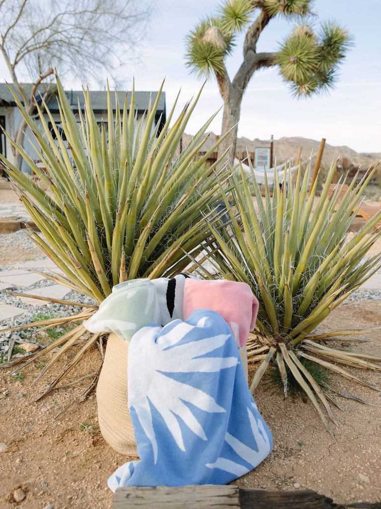 Blue and white, green and white, and pink and white tropical patterned cabana beach towels folded in a basket in the desert. 