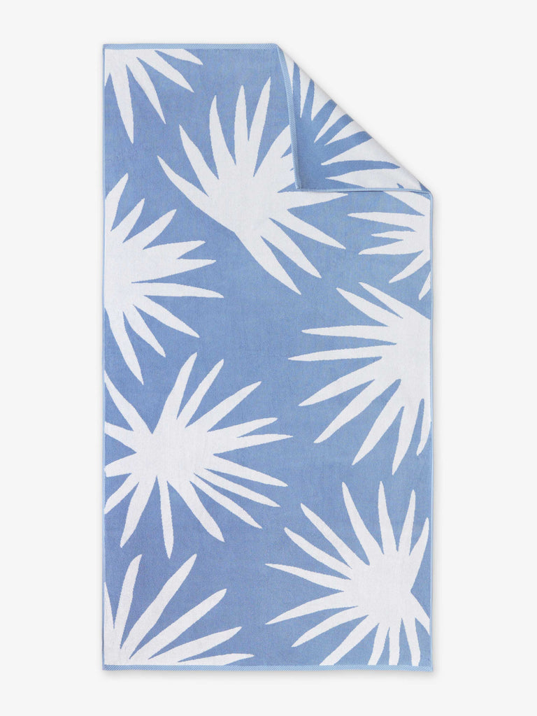 An oversized, blue and white palm tree patterned cabana beach towel laid out.