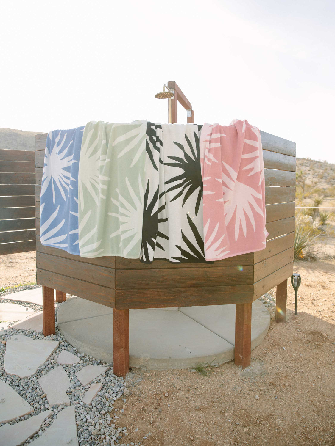 Blue and white, green and white, white and black, and pink and white tropical patterned cabana beach towels hanging over an outdoor shower.