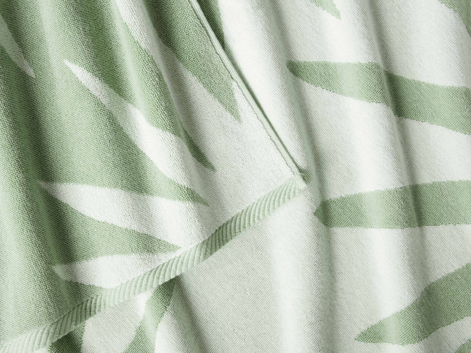 
      A close-up of a thick and soft, green and white tropical patterned cabana beach towel.
    