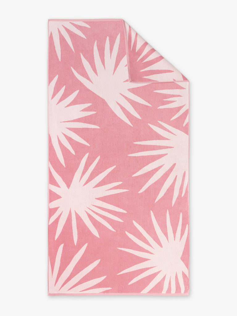An oversized, pink and white palm tree patterned cabana beach towel laid out.