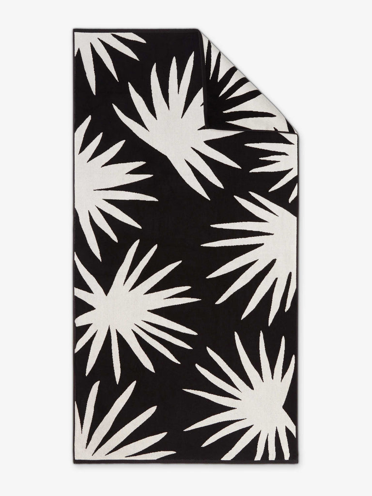 An oversized, black and white ivory palm tree patterned cabana beach towel laid out.
