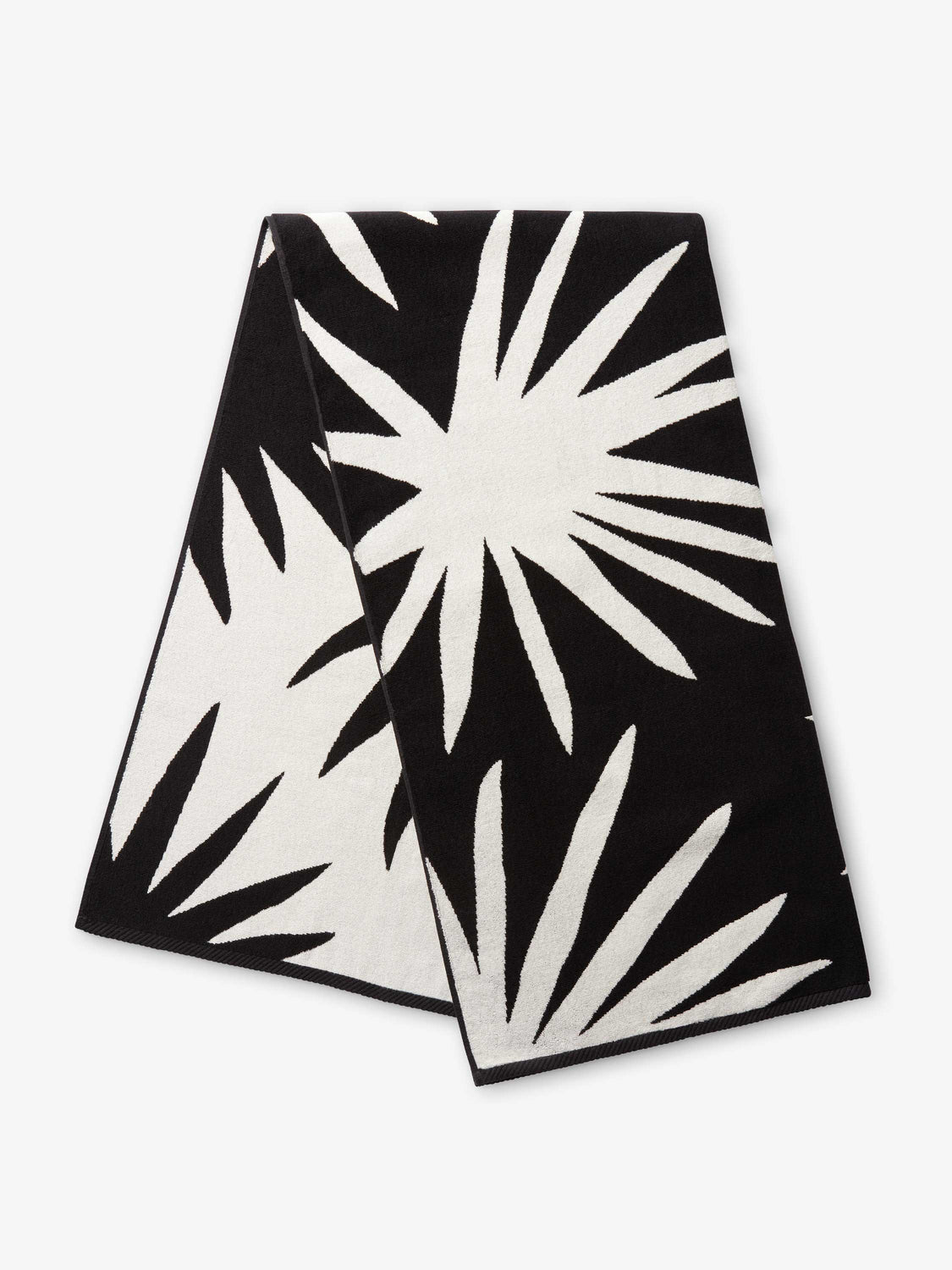 A folded black and ivory white tropical patterned cabana beach towel.
