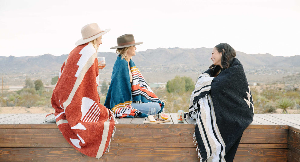 Three women wrapped for warmth in Mexican blankets in red, blue, and black.