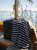 An extra absorbent, black and white striped cabana beach towel hanging over a black beach bag on a sailboat. 