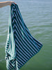 A woman holding out an extra large, green and white striped cabana beach towel over the water.
