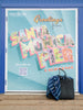 A navy blue, multicolor-striped towel in a black beach bag on the ground in front of a “Greetings from Santa Monica Pier California” sign.