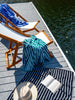 Oversized blue, green, and black striped cabana beach towels draped on chairs on a lake dock.