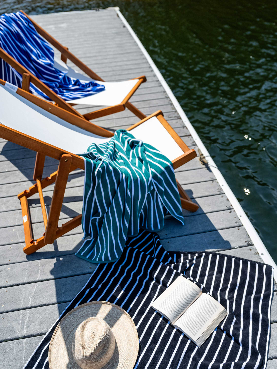 Blue, green, and black striped extra-large cabana towels draped on luxury deck chairs on a lake dock.