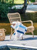 A photo of a white ivory and blue Mexican Blanket draped over a chair by the water.