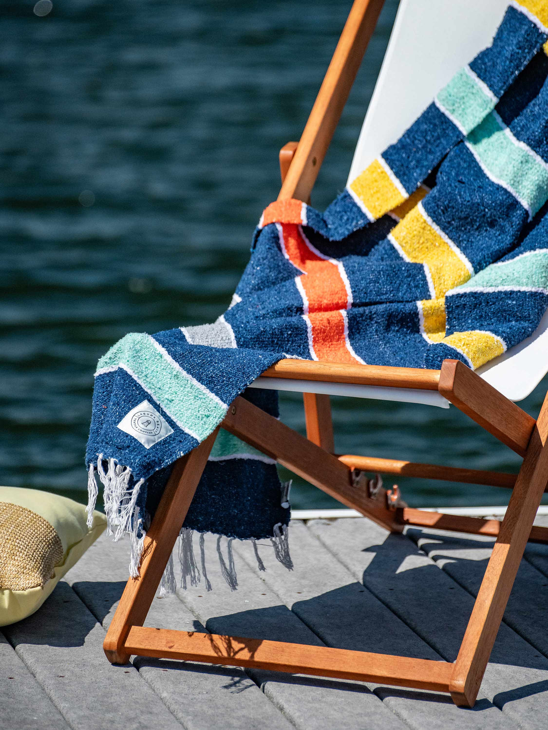 A multicolored striped Mexican Blanket draped over a chair by the water.