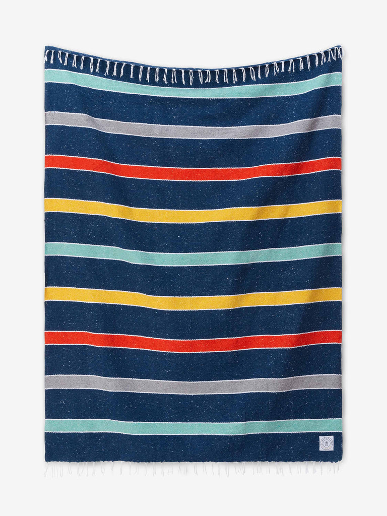 A multicolored blue, orange, and yellow striped Mexican Blanket with tassels laid out.
