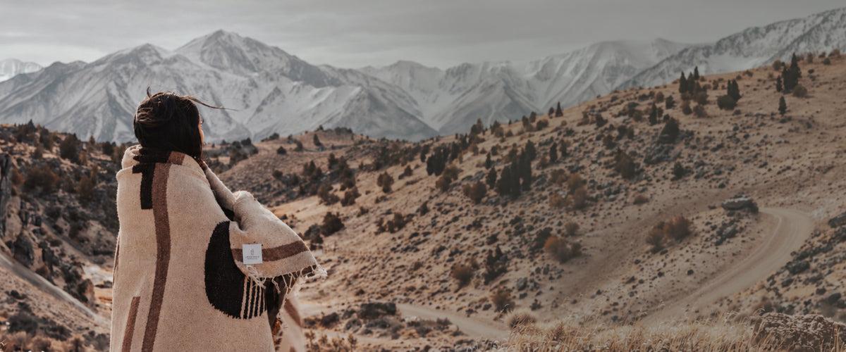 Wheat Sol Mexican blanket wrapped around a person overlooking snow-covered mountains.