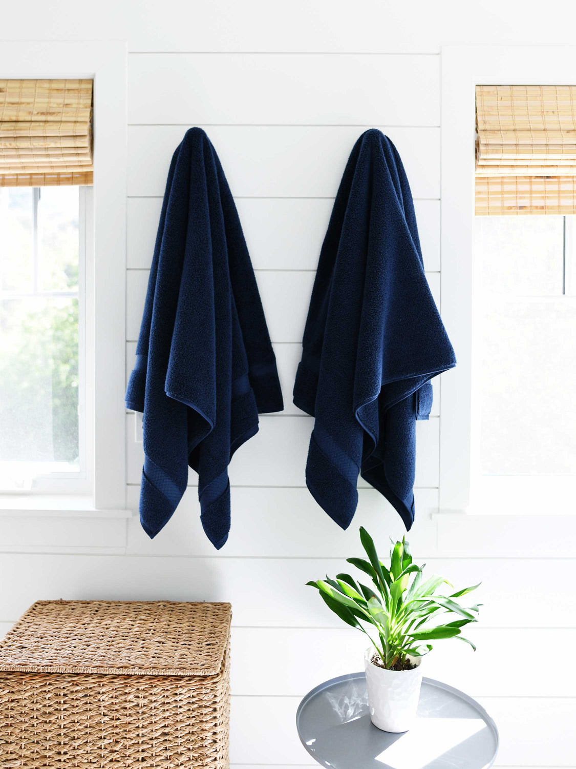 A pair of navy blue cotton bath towels hanging on a wall side by side.