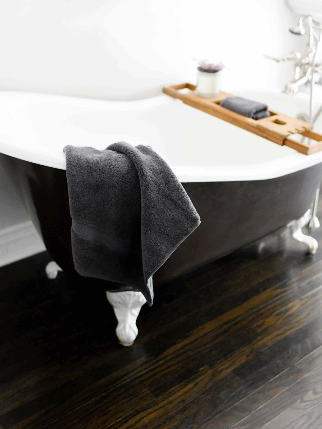 A dark gray cotton bath towel draped over the edge of a bathtub.