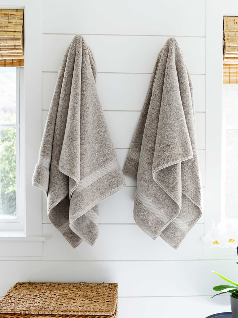 A pair of sand colored cotton bath towels hanging on a wall side by side.