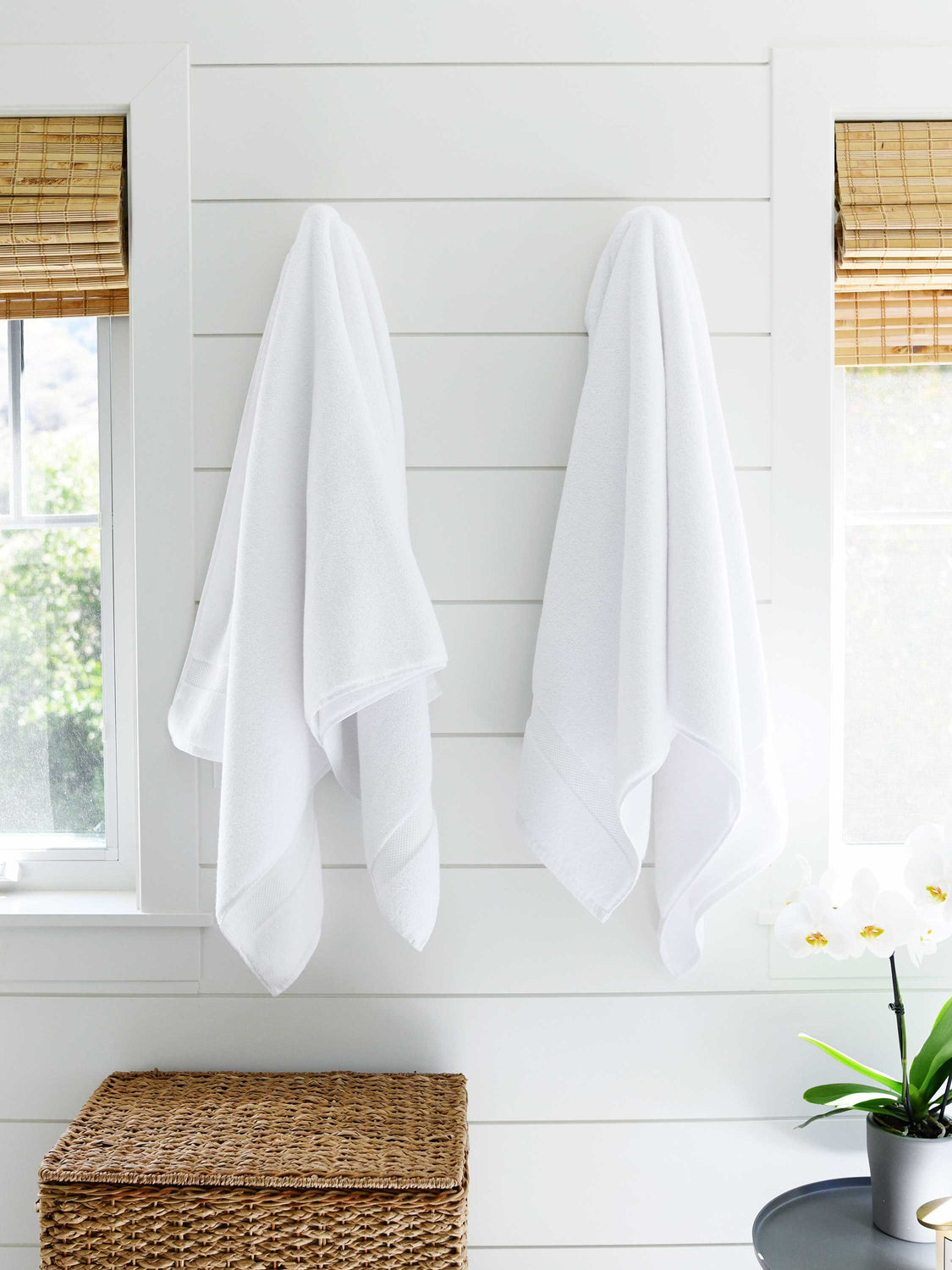 A pair of white cotton bath towels hanging on a wall side by side.