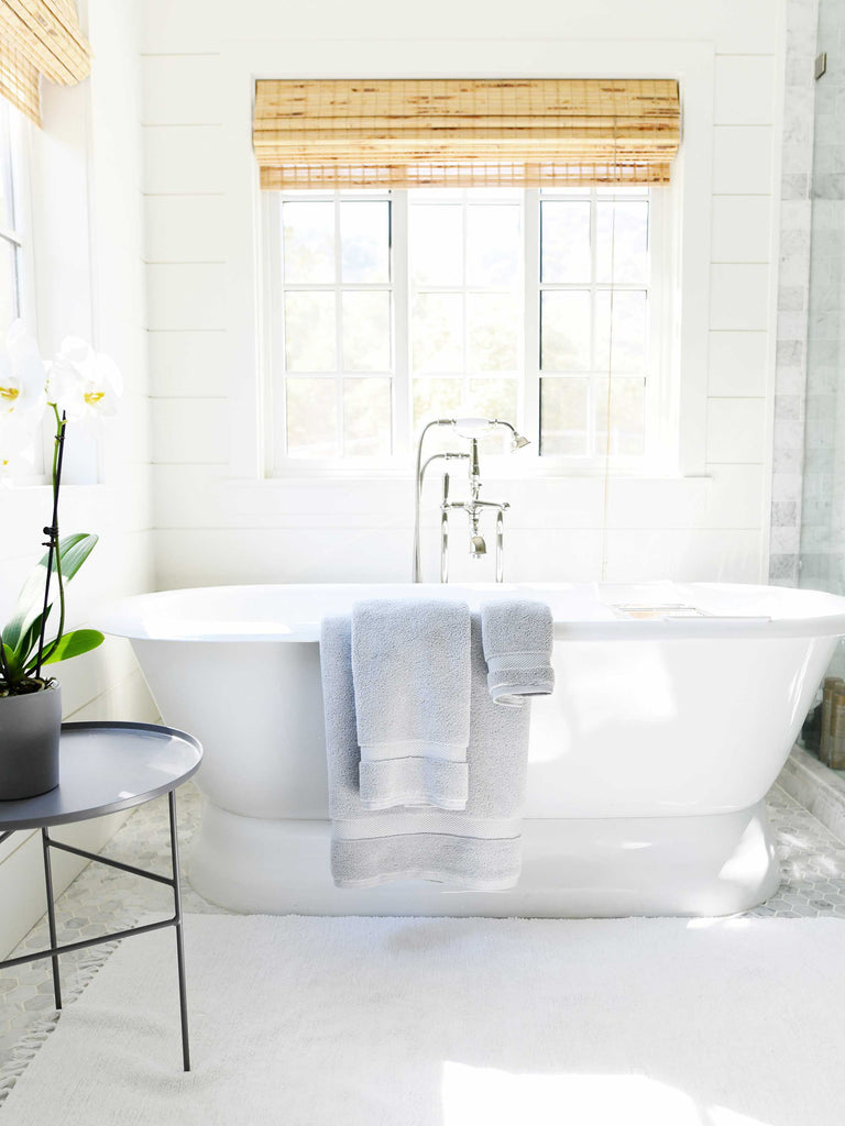 A set of gray cotton bath towels draped over the edge of a bathtub.