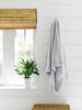 A gray cotton bath towel hanging on a wall next to a window.