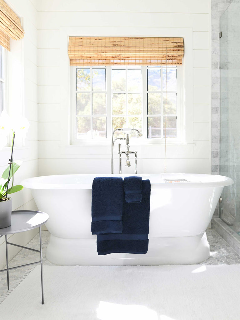 A set of navy cotton bath towels draped over the edge of a bathtub.
