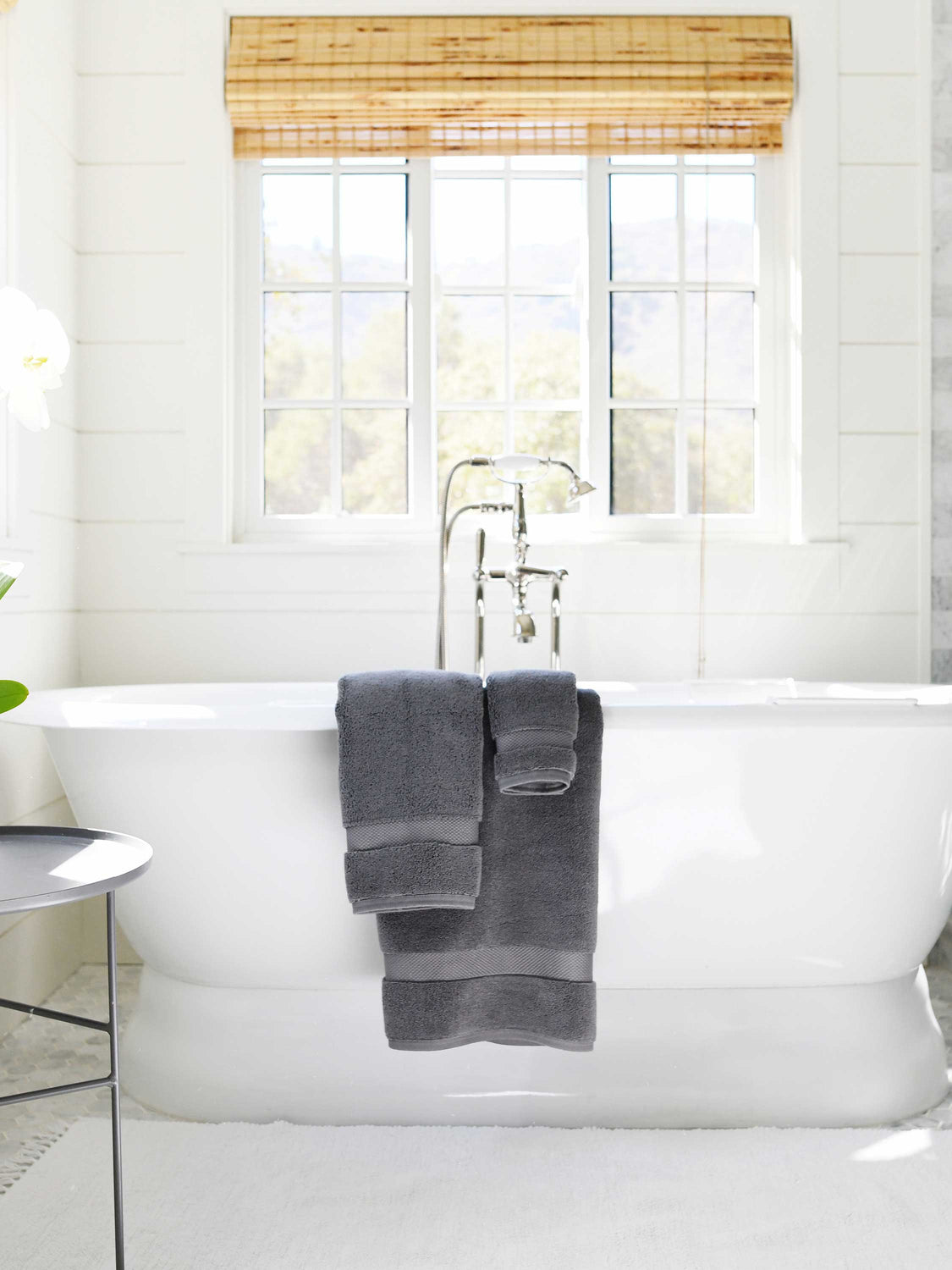 A set of dark gray cotton bath towels draped over the edge of a bathtub.