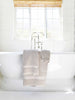 A set of tan cotton bath towels draped over the edge of a bathtub.