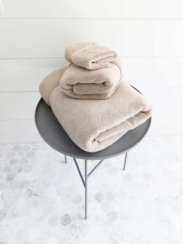 A set of tan cotton bath towels folded and stacked on one another on top of a side table.