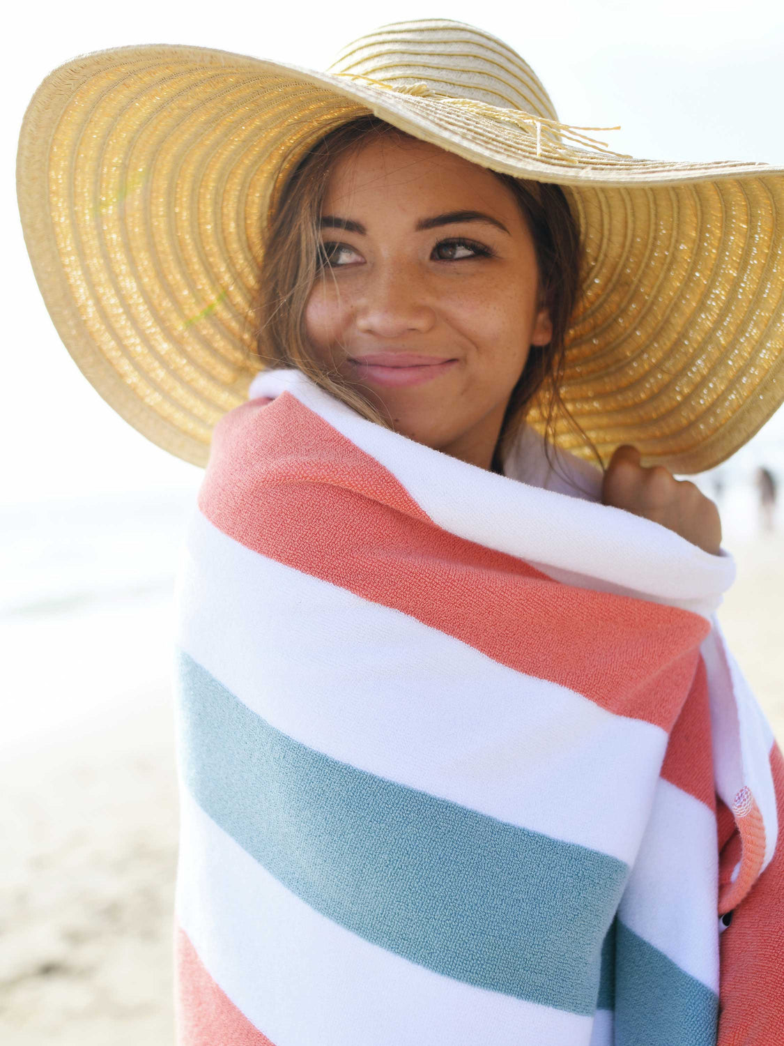A close-up of a woman wrapped in an orange, green, and white striped cabana beach towel.