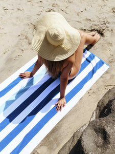 A woman laying out on a blue, green, and white striped cabana beach towel at the beach.