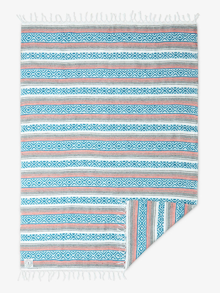 A traditional, hand-woven Mexican blanket in blue, pink, and gray with white fringe spread out.