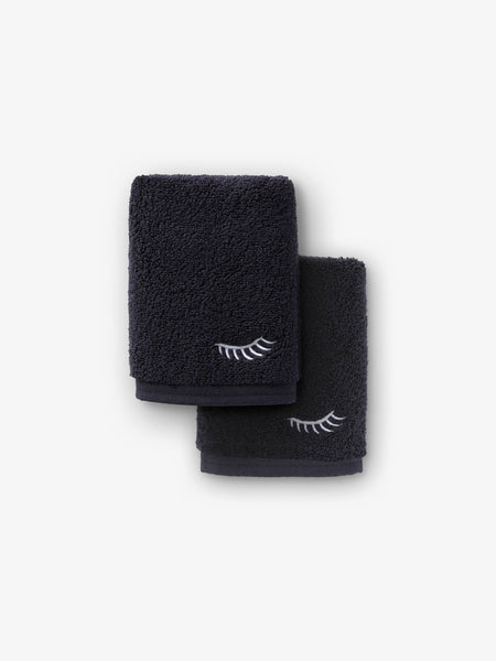 A pair of black makeup towels with a decorative eyelash embroidered in white.
