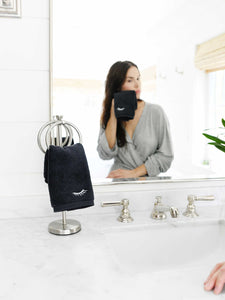 A woman drying her face with a black makeup towel looking in the mirror.