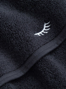 A close-up shot of a black makeup towel with an eyelash strip embroidered in white.