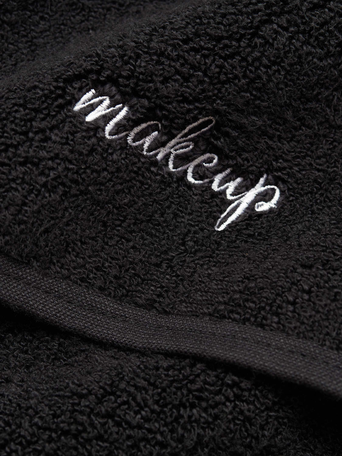 A close-up of a black makeup towel with the word "makeup" embroidered in white.